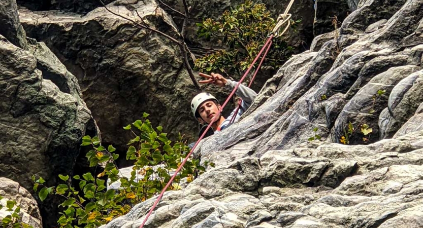 a student gives a peace sign while rock climbing